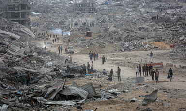 People walk on a road amid a landscape of destruction.