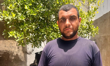 Portrait of a man standing in front of a wall with a tree growing behind it 