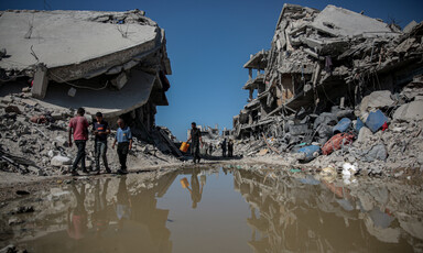 Several Palestinians in Jabaliya walk by standing water and demolished buildings