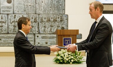 Israel's President Issac Herzog holds a leather-bound folder on one side as the European Union diplomat Michael Mann holds it on the other side.