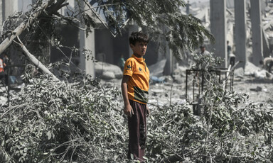 A boy wearing a bright yellow shirt stands in contrast to dust-covered environment around him