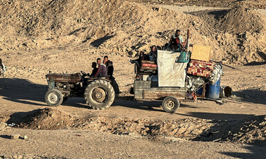 A tractor carries people and belongings along a sandy path