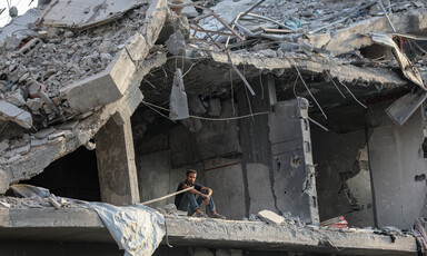 A man sits on an upper floor of a concrete building that no longer has walls or a facade.