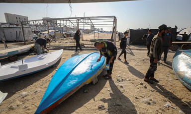 A man sands the bottom of a small fishing vessel