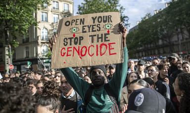 Man holds up cardboard sign with painted letters reading "Keep your eyes on the Genocide"