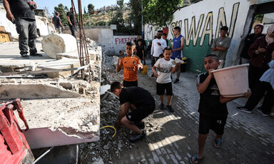 A boy holds a bucket beside other children and some adults next to a demolished building in occupied East Jerusalem 