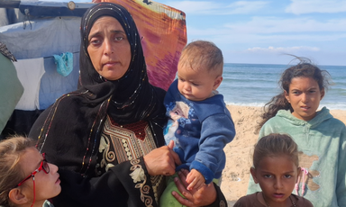 A woman stands with her children with the sea behind her