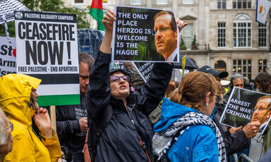 Protesters in London hold up a placard showing a photograph of Israel's President Isaac Herzog beside captions arguing that he should be in The Hague on war crimes charges