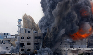 A massive plume of smoke and flames erupt from a partially-destroyed building