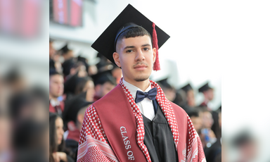 Young man wearing graduation cap and kuffiyeh is seen from chest up