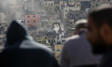 A bulldozer demolishing homes with men watching