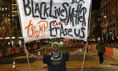 A protester holds a banner reading Black Lives Matter Trump Can't Erase Us
