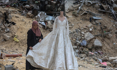 a woman displaying a mannequin in a white wedding dress, surrounded by piles of sand and rubble