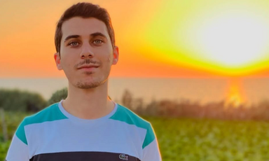 A yellow-orange sun and sky shines behind a young man, smiling. 