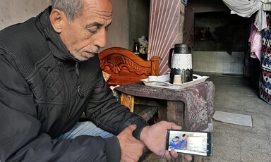 a man sitting on a bed and holding a phone while displaying an image to the camera