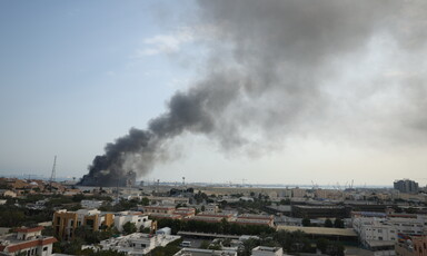 A wide urban landscape with thick smoke rising from a large building