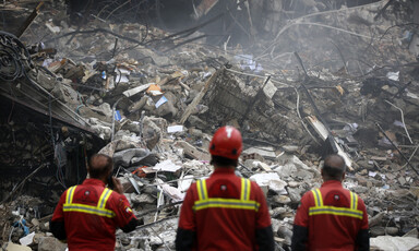 Three first responders stand in front of badly damaged building.