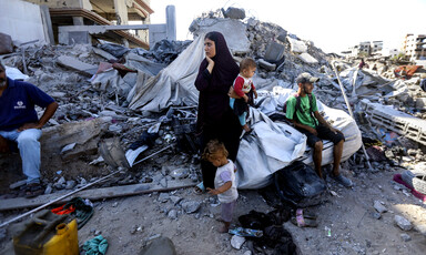 A young woman holds her hand to her face while holding a toddler with a man and young child standing and sitting next to her