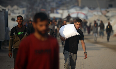 A man carries a white bag of flour over his shoulder.