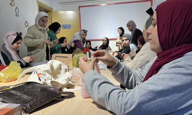 A group of women sitting around a table and some of them are making accessories from beads.