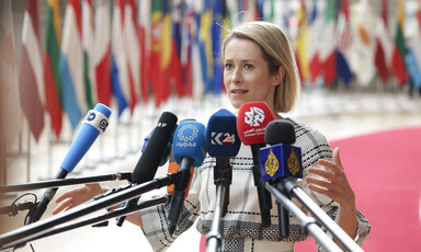 European Union representative Kaja Kallas stretches out her arms as she stands behind several microphones of television channels 