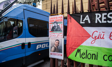 Posters with photographs of two Palestinian prisoners beside a blue Italian police van and a Palestinian flag