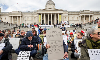 A large number of people sit in the Trafalgar Square area of London and hold placards bearing such slogans as I oppose genocide I support Palestine Action