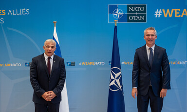 Two men stand in front of flags. 