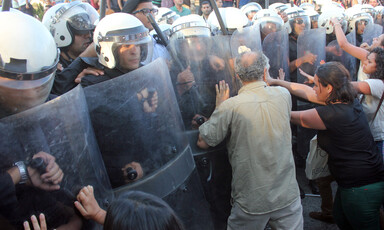 Protesters push at shields held by police wielding batons. 